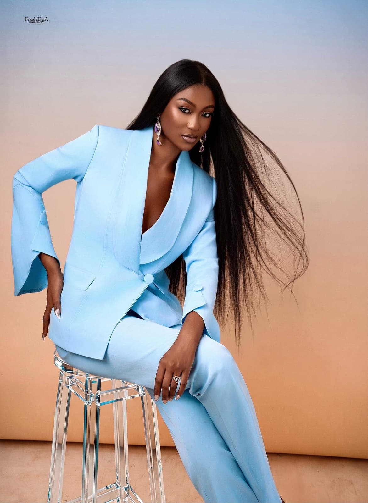 Woman in a tailored sky-blue Moirai power suit, seated against a peach backdrop