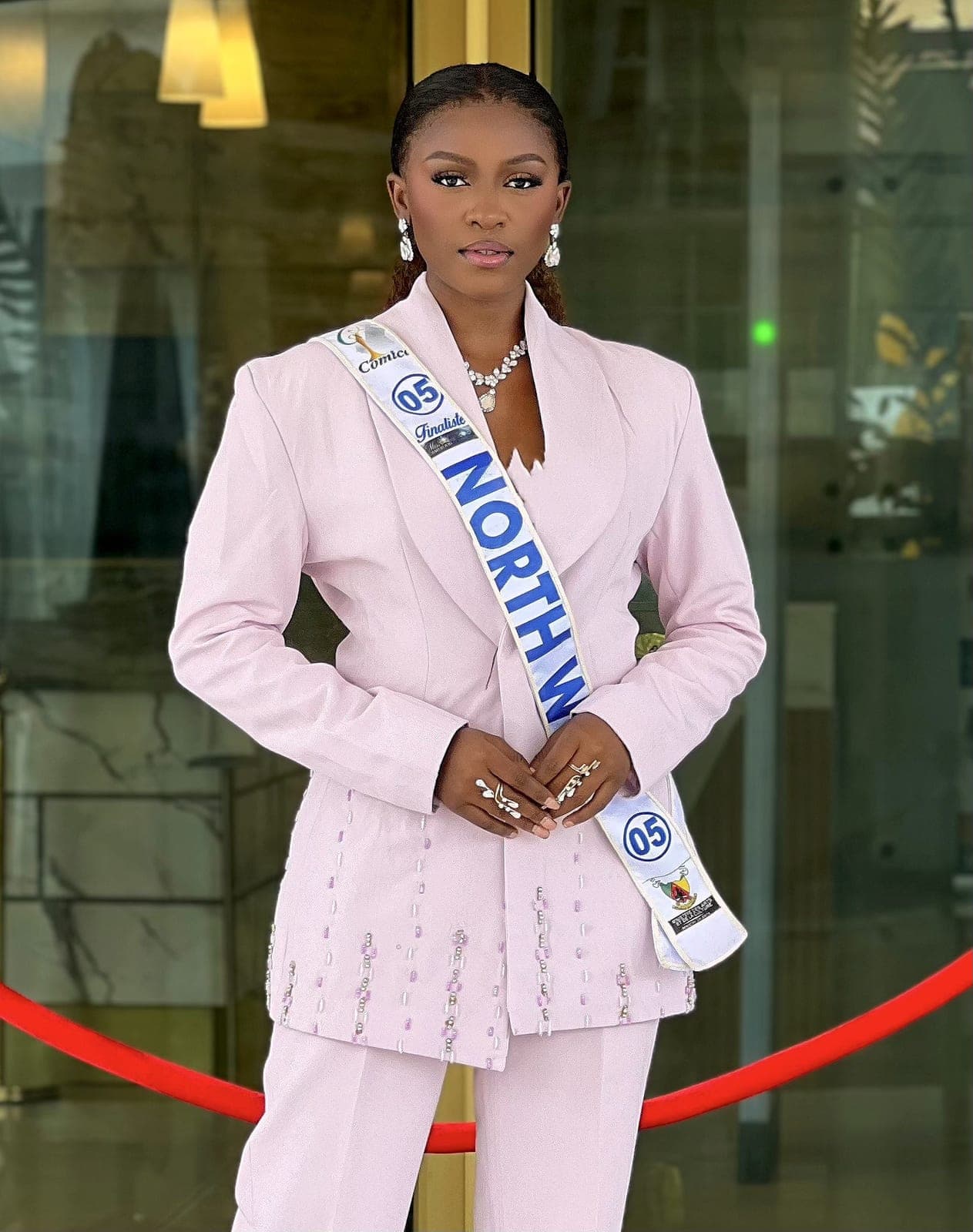 Pageant contestant in a tailored blush-pink Moirai suit with an embellished jacket and North West sash