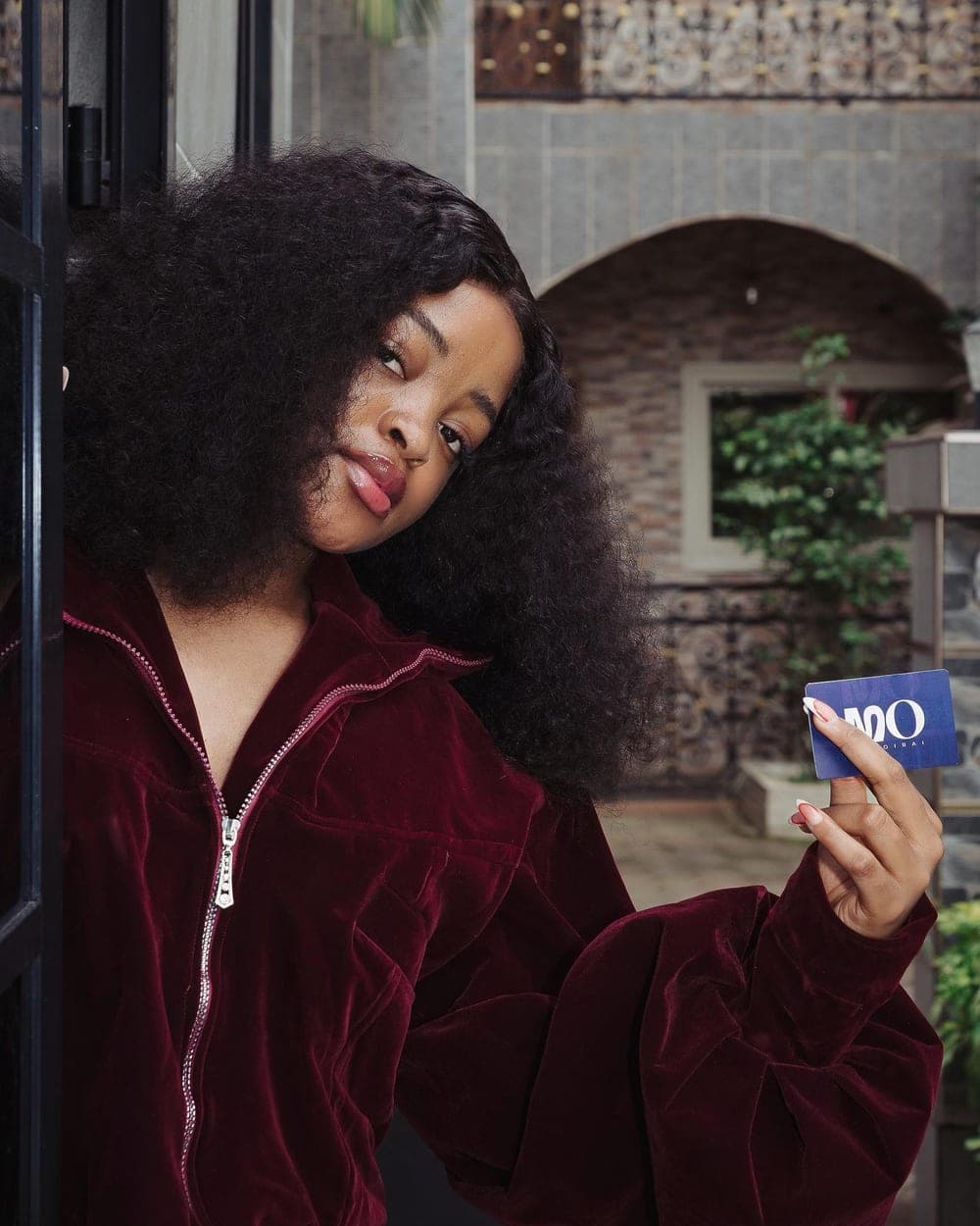 Velvet Puff STASIS — woman in a burgundy zip-front velvet puff jacket holding an MO card